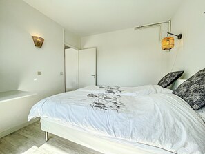 Un dormitorio con cama, dos luces fijadas a la pared, una puerta y una pared blanca.