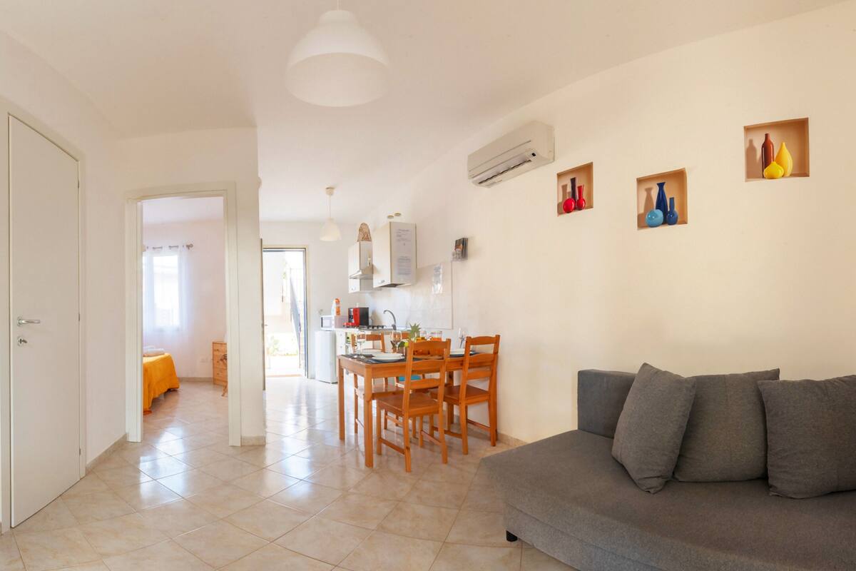 A modern living room with a grey sofa and a dining area with wooden chairs and a table.