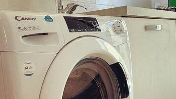 Una lavadora de carga frontal con panel de control, dosificador de detergente e toma de agua.