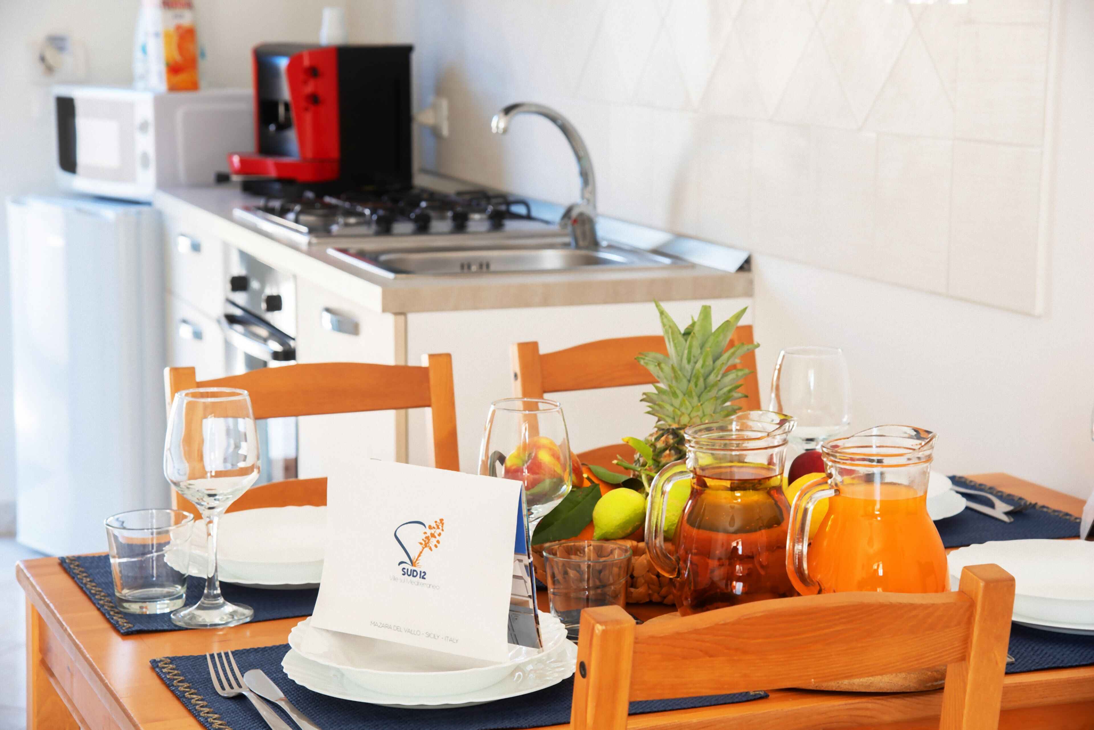 Una mesa con sillas, una cafetera, un fregadero y electrodomésticos de cocina.