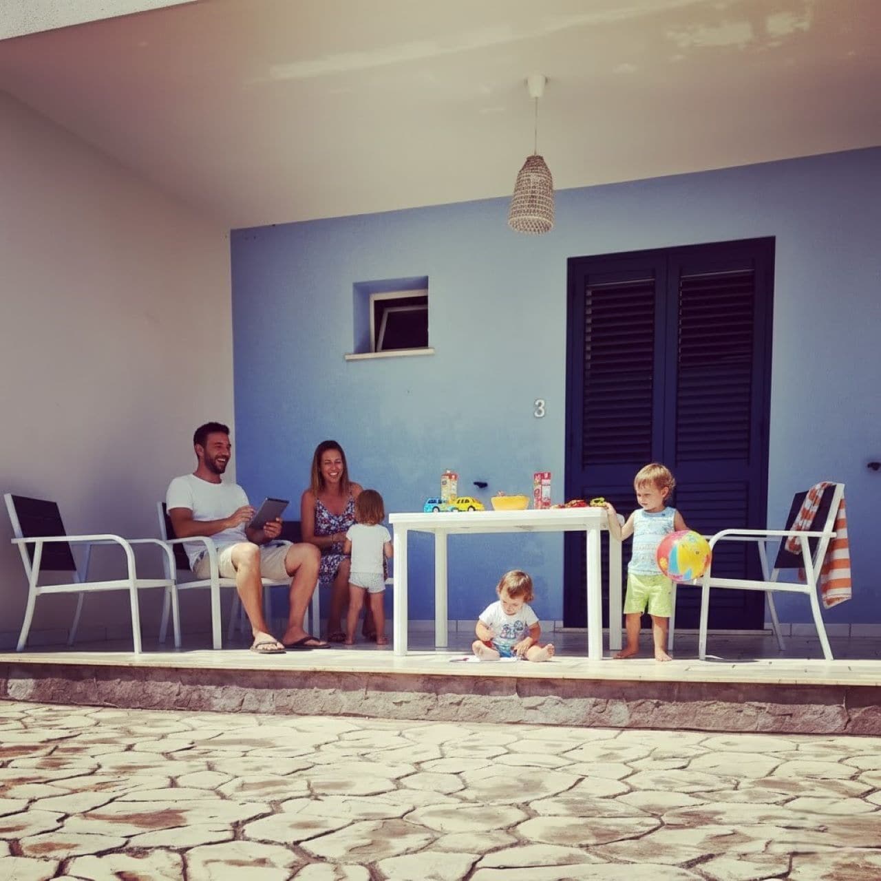 A family of four seated at a table with a view of a blue wall and a window.