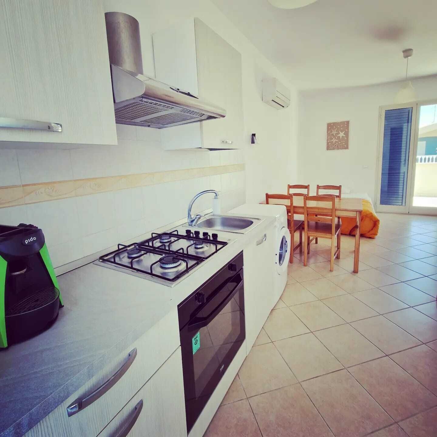 Una cocina compacta con estufa a gas, horno y lavadora, un comedor con mesa y sillas, y un amplio ventanal que proporciona luz natural.