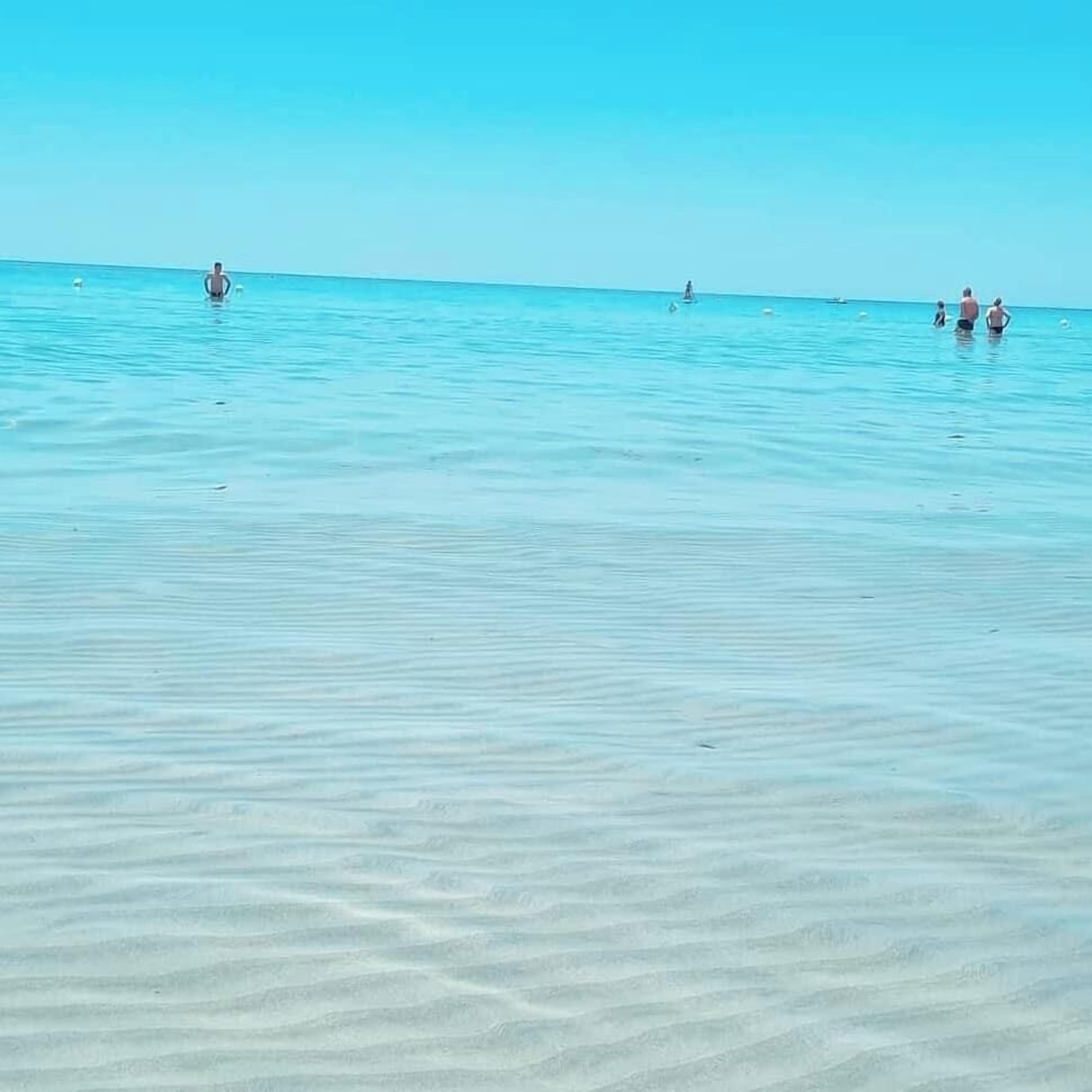 Una spiaggia con acque turchesi limpide e disegni nella sabbia ben visibili.