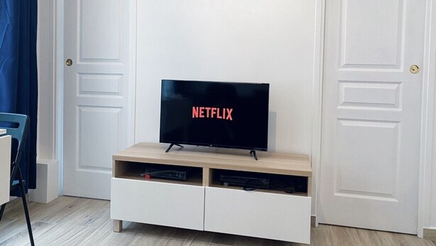 A room with a TV on a wooden stand, a blue curtain, and white doors.