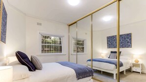 A bedroom with a large mirror, two beds, a window, and a nightstand with a lamp.