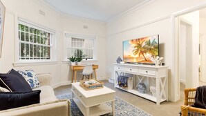 A living room with a white sofa, a coffee table, a TV, and a painting of a beach scene.