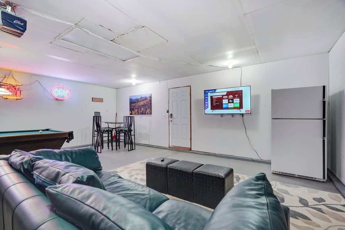 A modern lounge area with a pool table, leather sofa, and a flat-screen TV mounted on the wall.