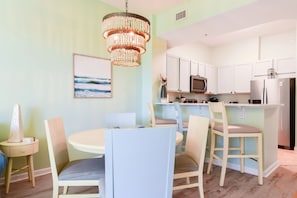 A dining area with a round table and chairs, a chandelier, and a kitchen with white cabinets and appliances.