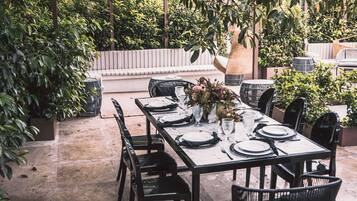 An outdoor dining area with a table set for four, surrounded by chairs, under a pergola with hanging baskets.