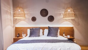 Un lit bien fait, avec une couette blanche et grise, deux tables de chevet avec des lampes et une tête de lit en bois.