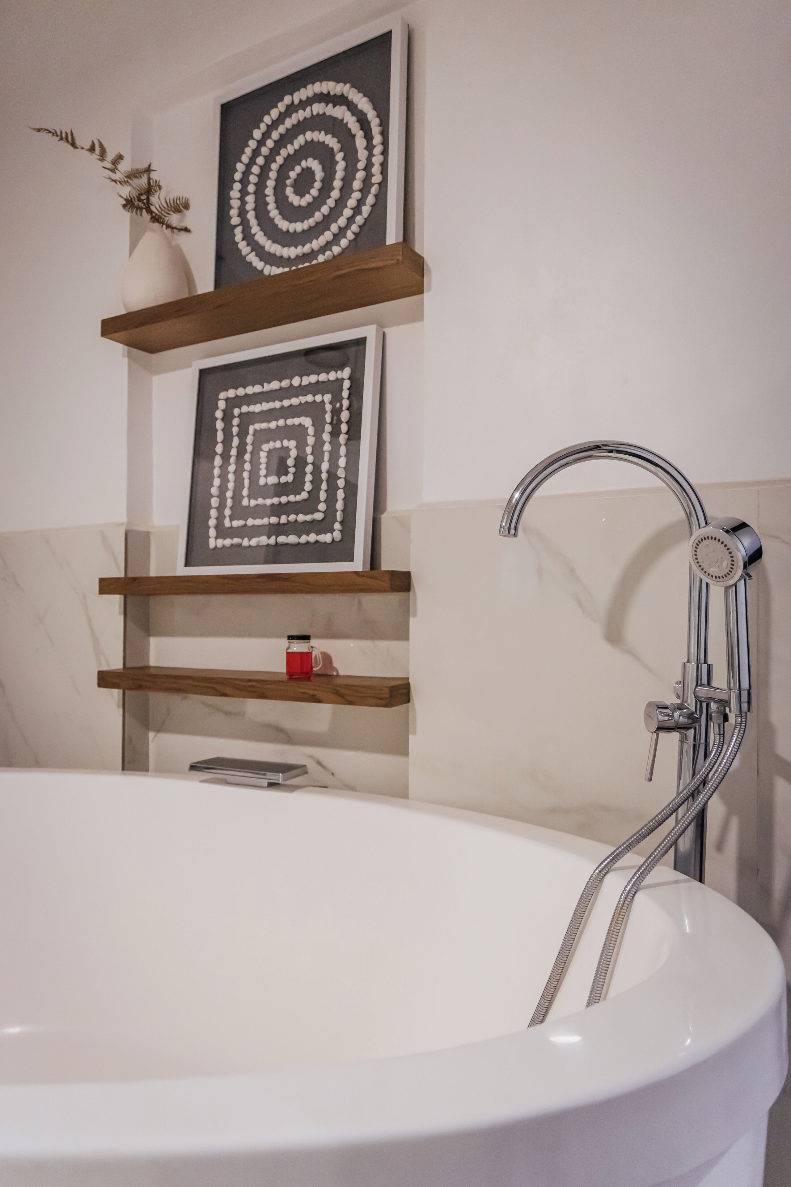 A modern bathroom with a freestanding bathtub, wooden shelves with decorative items, and a showerhead.