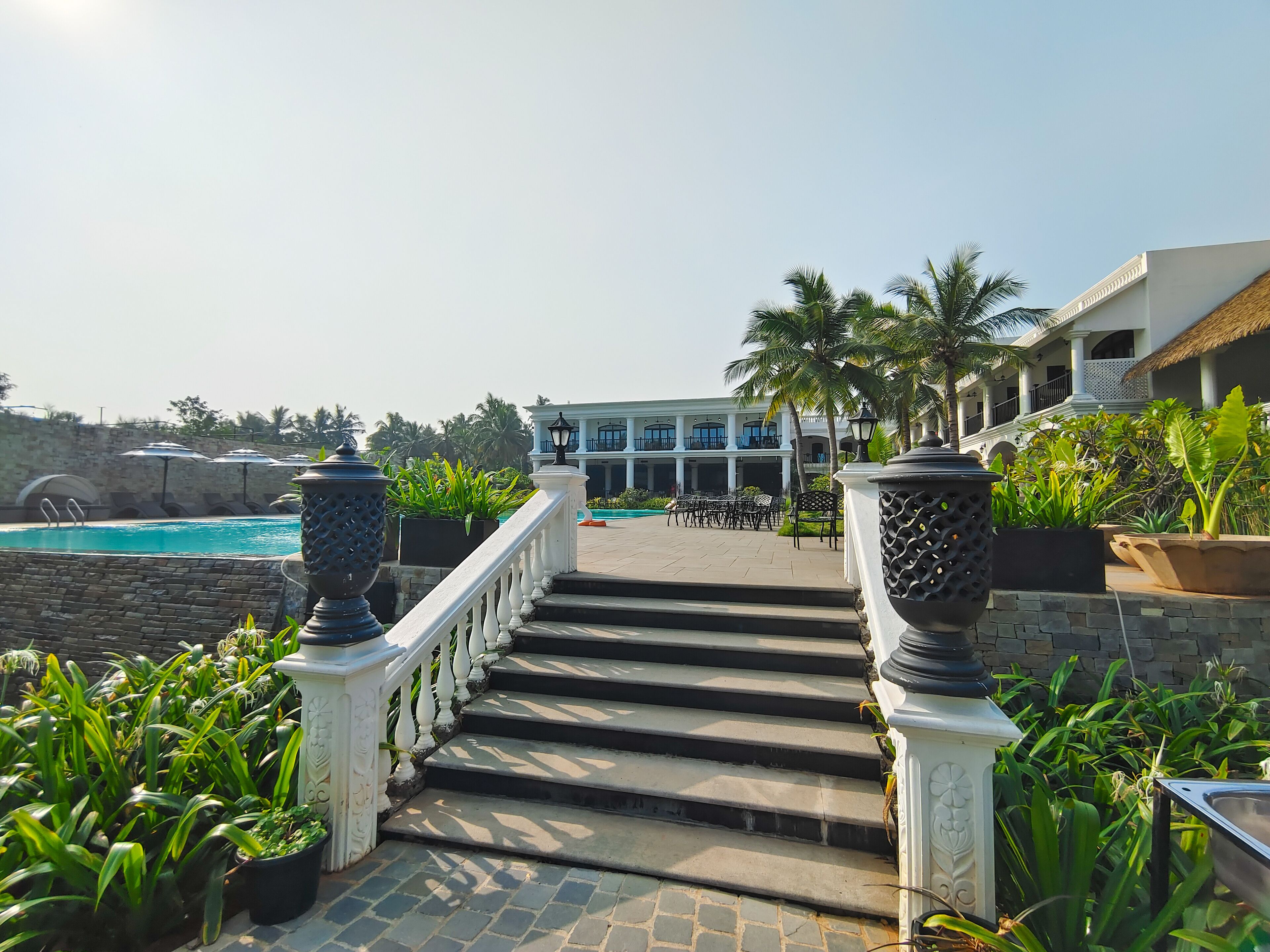 A staircase leading to a pool area with outdoor seating and palm trees.