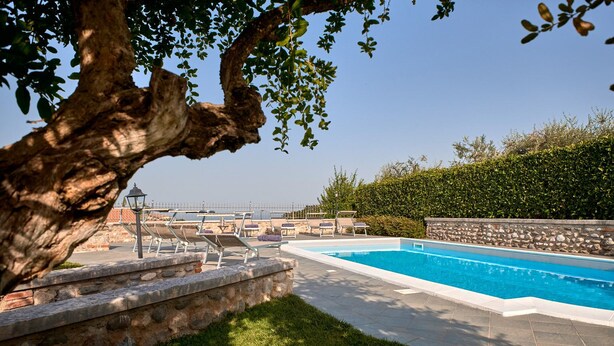 A swimming pool with lounge chairs, a stone wall, and a view of the sea. - Villa Ardea Exclusive Holigarda (Soiano del Lago)