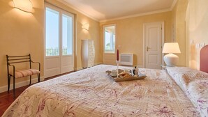 A bedroom with a large bed, a chair, a dresser, a lamp, and a tray with breakfast items. - Villa Ardea Exclusive Holigarda (Soiano del Lago)
