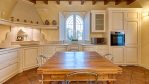 A spacious kitchen with a large wooden table, white cabinetry, and a built-in oven. - Villa Ardea Exclusive Holigarda (Soiano del Lago)