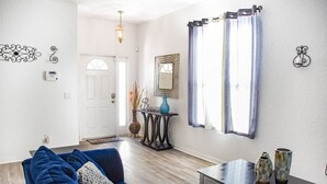A living room with a blue sofa, a small table with vases, a decorative mirror, and a door leading to another room. - HR135HS - Highlands Reserve - 4 beds pool home close to Disney (Davenport)