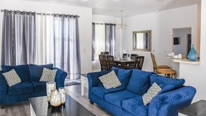 A living room with two blue sofas, a coffee table, and a dining area with a chandelier. - HR135HS - Highlands Reserve - 4 beds pool home close to Disney (Davenport)