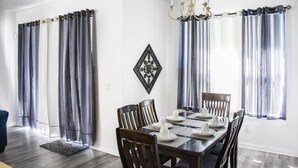 A dining room with a wooden table set for four, flanked by curtains and a chandelier. - HR135HS - Highlands Reserve - 4 beds pool home close to Disney (Davenport)