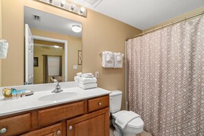 Une salle de bain avec un lavabo blanc, un meuble-lavabo en bois et un rideau de douche à motifs géométriques.