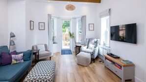 Una sala de estar moderna con un sofá azul, un reposapiés estampado, un sillón de cuadros y un televisor sobre un mueble de madera.
