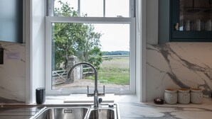 Una cocina con un lavamanos doble, una ventana con vistas al paisaje rural y una encimera de mármol.