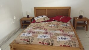 En säng med ett påslakan med ”resor”-tema, två sängbord med lampor och en sänggavel i trä.