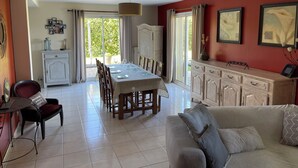 A spacious living area with a dining table set for four, a sofa, and a cabinet with decorative items. - Maison Familiale " L'abbé Garo " (Port-en-Bessin-Huppain)