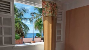 A room with a window overlooking a beach, a small stool, and a potted plant. - Balaou Villa facing the sea (anse d'arlet)