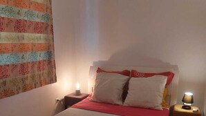 A neatly made bed with a red blanket, two bedside tables with lamps, and a floral curtain. - Balaou Villa facing the sea (anse d'arlet)