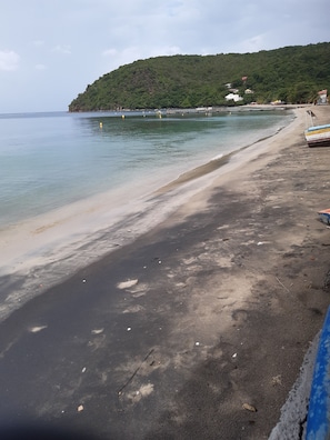 A beach with a sandy shore, a pier extending into the water, and a hill with buildings in the background. - Balaou Villa with a View of the Sea (anse d'arlet)