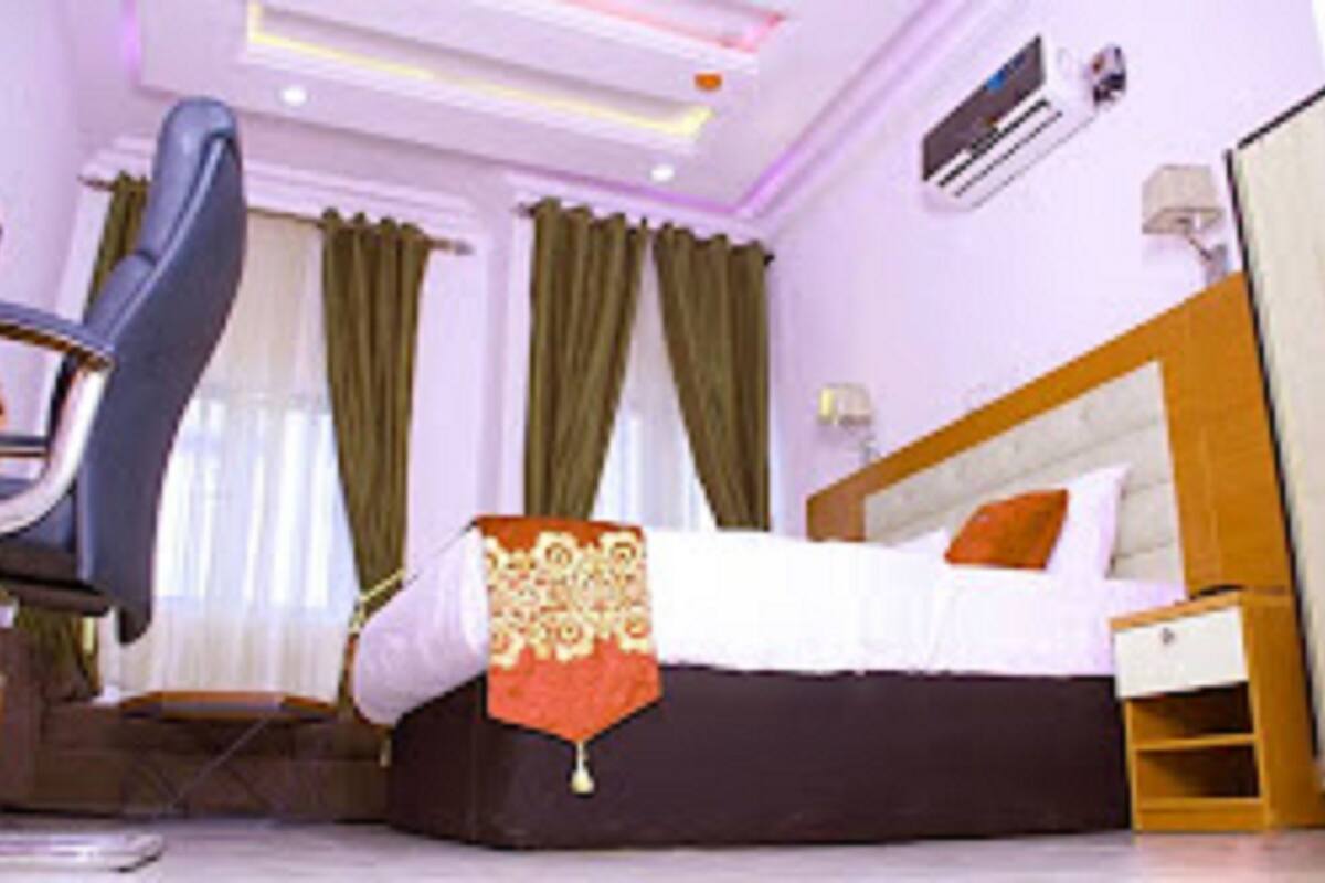 A hotel room with a bed, a chair, a nightstand, and an air conditioning unit.
