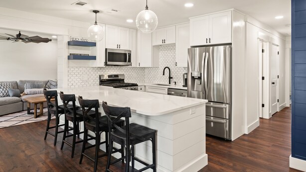 Une cuisine moderne avec des meubles blancs, un grand îlot central, des appareils électroménagers en acier inoxydable et un ventilateur de plafond.