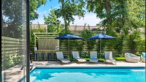 Une piscine entourée d’une clôture en bois et d’arbres, avec des chaises longues et des parasols à proximité.