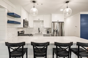A modern kitchen with white cabinets, a large island, black chairs, and pendant lighting.