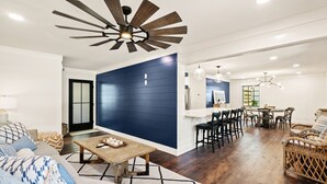 Un salon moderne avec un mur d’accent bleu foncé, un plancher en bois et un ventilateur de plafond.