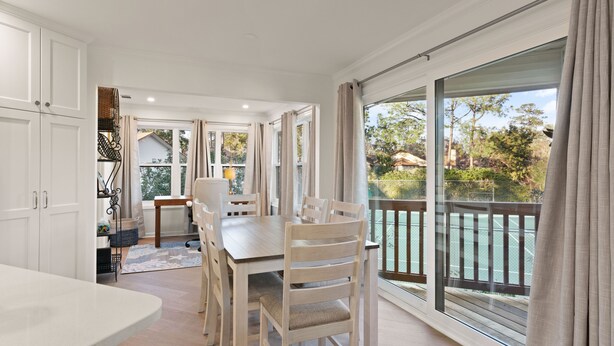 Ein Essbereich mit großem Tisch und Stühlen, Blick auf einen Pool durch große Fenster sowie ein Balkon mit Geländer.