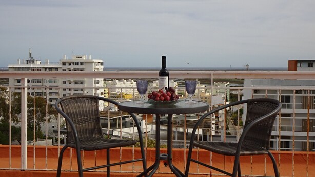 Un balcón con una mesa preparada para dos personas, que incluye una botella de vino, un bol de uvas y dos copas.