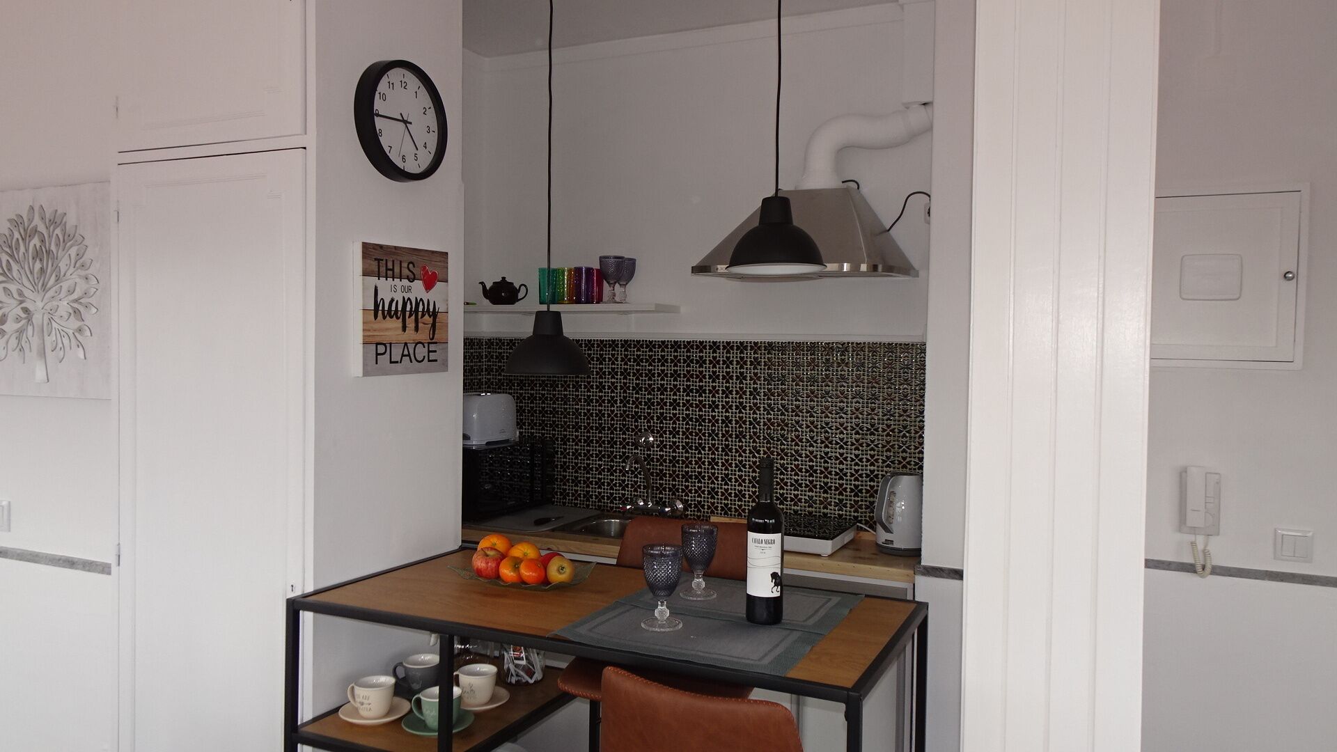 A compact kitchen with a dining area, a clock, and a decorative sign.
