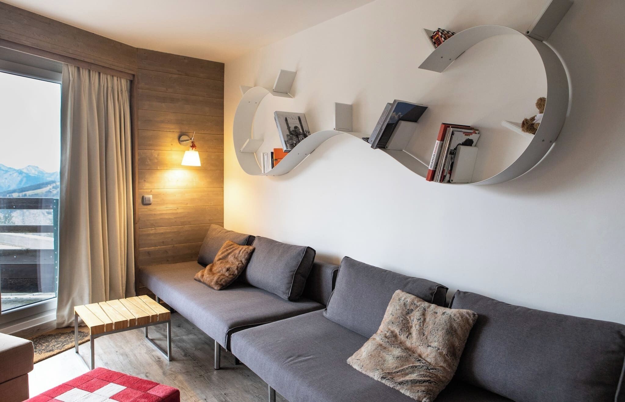 A modern living room with a grey sofa, a wooden bench, and a red and white rug.