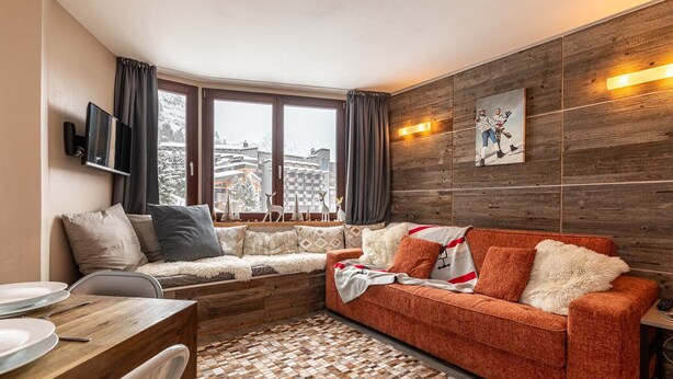 Una sala de estar acogedora con una pared de madera, un sofá, un televisor y vistas a edificios cubiertos de nieve.