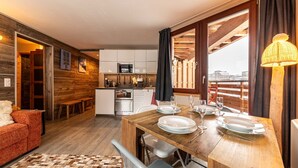 Una habitación acogedora y bien iluminada con una mesa de madera para cuatro personas, un sofá y una cocina al fondo.