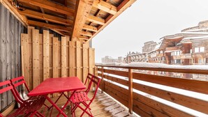Un balcón de madera con una mesa y sillas rojas, con vista a un pueblo nevado.