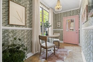 Ein Zimmer mit Wandtapete mit Muster, ein Holzstuhl, eine rosafarbene Tür und eine Chandelüster.