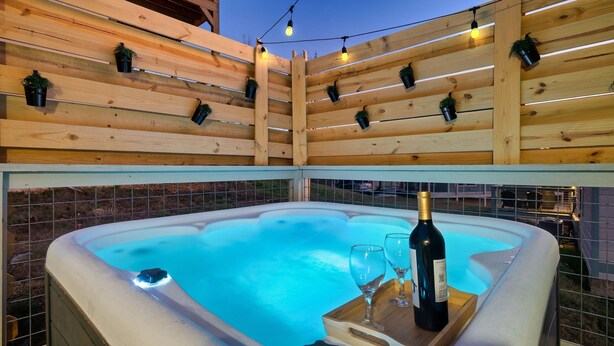 Un jacuzzi con cubierta de madera y luces colgantes, rodeado por una valla.