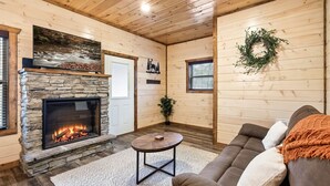 Un interior de cabaña acogedor con una chimenea de piedra, un sofá cómodo y una pequeña mesa redonda.
