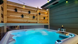 Un jacuzzi con cubierta de madera, una botella de champán y dos copas sobre una bandeja.