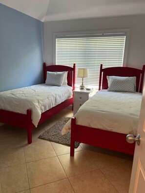 Two single beds with red headboards and white bedding, a bedside table, and a lamp.