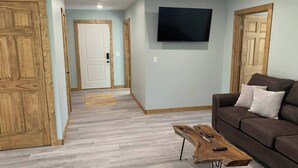 A living room with a brown sofa, a wooden coffee table, and a flat-screen TV mounted on the wall.
