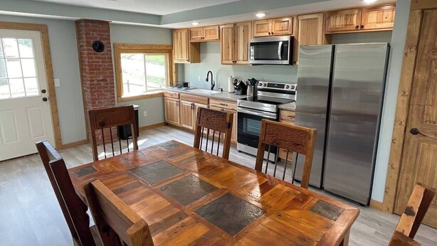 A modern kitchen with wooden cabinets, a stainless steel refrigerator, and a dining table with chairs.