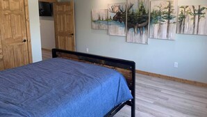 A bedroom with a bed, wooden wardrobe, ceiling fan, and wall-mounted paintings.
